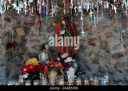 Angebote der Kruzifixe und Kerzen in einer kleinen künstlichen Grotte bei El Santuario De Chimayo, New Mexico. Die Kirche und die Anlage ist ein Bereich der Wallfahrt Stockfoto