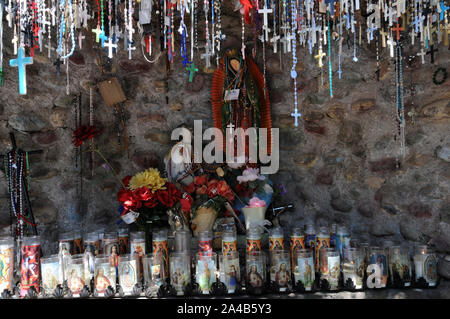 Angebote der Kruzifixe und Kerzen in einer kleinen künstlichen Grotte bei El Santuario De Chimayo, New Mexico. Die Kirche und die Anlage ist ein Bereich der Wallfahrt Stockfoto