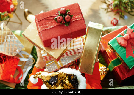 Urlaubszeit. Obere Ansicht der elegante Frau in glitzern gold Pailletten Weihnachtsmütze mit Haufen von Weihnachtsgeschenk Kisten mit Sofa im modernen Leben Stockfoto