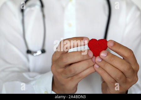 Kardiologie und Gesundheit, Arzt halten roten gestrickt Herz in den Händen in der Nähe der Brust. Kardiologe, Blutspende, Behandlung von Herzerkrankungen Stockfoto