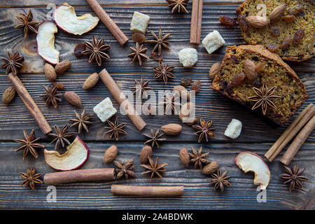 Hausgemachte würziger Kürbiskuchen Schichten mit Walnüssen, brauner Zucker, Anis Sterne, Rosinen, getrocknete Äpfel, Nelken, Zimt auf rustikalen Holzmöbeln braunen Hintergrund. Stockfoto