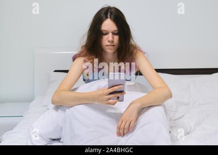 Müde Teenager Mädchen zu Hause im Bett sitzen am Handy suchen. Stockfoto