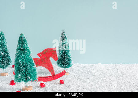 Weihnachten Hintergrund. Tannen mit Pferd, Spielzeug und roten Beeren auf Schnee Hintergrund. Kreative Weihnachtskarte mit Kopie Raum Stockfoto