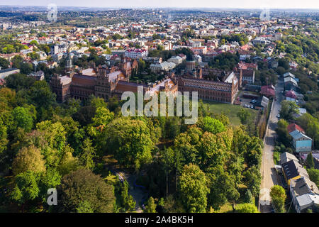 Greon alten Gebäuden der Czernowitzer Universität mit Türmen und Kuppeln zwischen grünen Bäumen und Häusern am Himmel Hintergrund in der Ukraine. Sun ist auf glänzenden Stockfoto