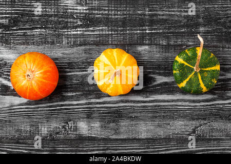 Herbst minimalistische Komposition mit Orange, Gelb und Grün Kürbisse auf dunklem Hintergrund. top anzeigen. Flach Stockfoto