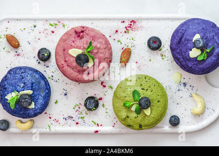 Hausgemachte raw vegan bunten Kuchen mit Matcha, Acai, blau Spirulina und butterfky Erbse Tee, frische Beeren, Minze, Muttern. Gesunde vegane Ernährung Konzept. nach oben Stockfoto