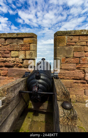 Alte schwarze Kanone durch eine Öffnung, die in einem Schloss Wall mit dem Meer im Hintergrund Stockfoto