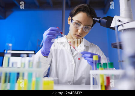 Low Angle Porträt der jungen Wissenschaftlerin Vorbereitung Blutprobe mit Dropper, während auf die medizinische Forschung im Labor Stockfoto