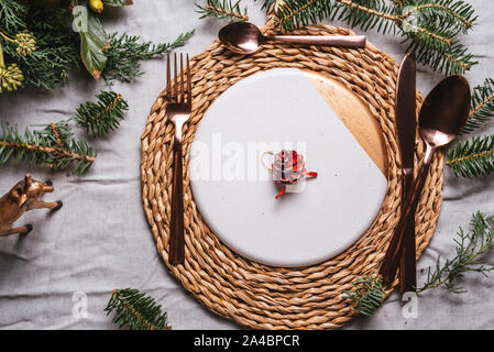 Weihnachten Tabelle Einstellungen mit einem Kranz, kiefer Zweig und goldenes Besteck von oben, Urlaub Abendessen Stockfoto