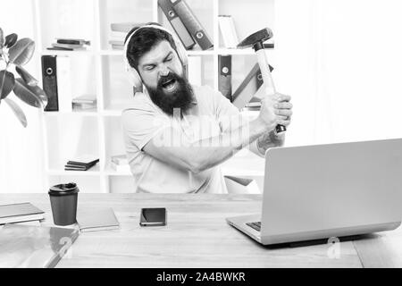 Veraltete Software. Computer lag. Gründe für Computer zurückbleiben. Wie fix langsam hinterher. Hasse office Routine. Man bärtige Kerl Kopfhörer Büro schwingen Hammer auf dem Computer. Langsame Internetverbindung. Stockfoto