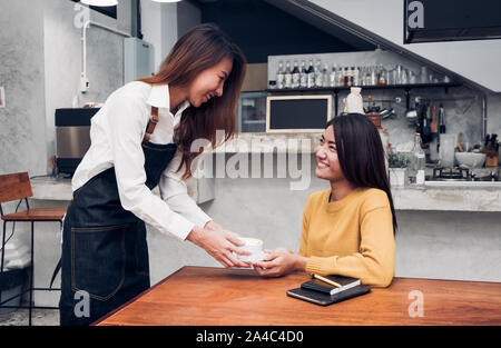 Junge asiatische Frau barista halten Kaffee Tasse ein Client im Coffee Shop serviert, start small Business Owner Essen und Trinken Konzept. Stockfoto