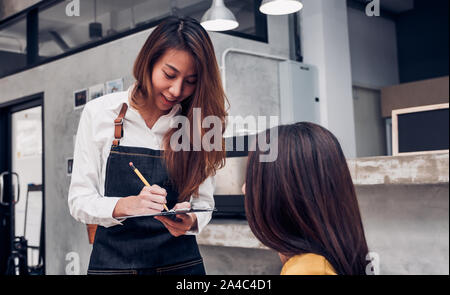 Jungen asiatischen barista Bestellung vom Kunden in ein Cafe, Cafe Besitzer schreiben Drink an der Bar, Essen und Trinken Business Konzept Stockfoto