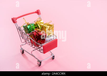 Jährliche Verkauf, Weihnachtsgeschäft Konzept - mini Rot Warenkorb Trolley voller Gift box auf rosa Hintergrund, kopieren Platz, in der Nähe Stockfoto
