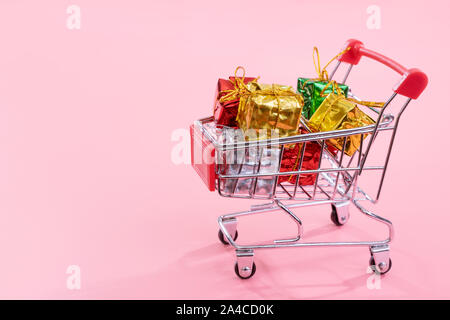 Jährliche Verkauf, Weihnachtsgeschäft Konzept - mini Rot Warenkorb Trolley voller Gift box auf rosa Hintergrund, kopieren Platz, in der Nähe Stockfoto