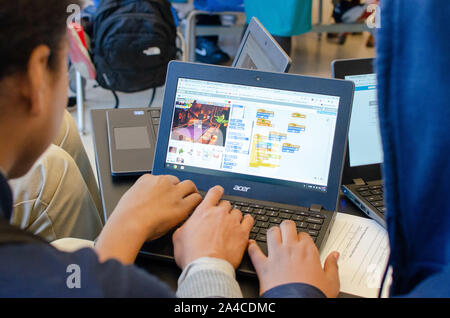 Drei Farbschüler in einer MINT-Highschool, die ein Notebook verwenden, um ein Spiel mit einer Entwicklersoftware zu programmieren und zu programmieren Stockfoto