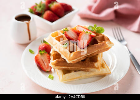 Leckere belgische Waffeln mit Erdbeeren auf weiße Platte mit Schokoladensauce serviert. Süßes Frühstück. Rosa Hintergrund, selektiver Fokus Stockfoto