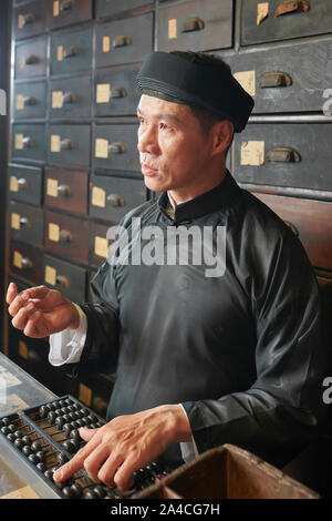 Reifen asiatischer Mann mit Abacus beim Zählen der Preis der Kräuter und Medizin in der alten Apotheke Stockfoto