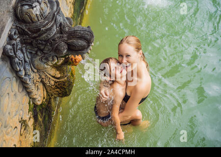 Mutter und Sohn Reisende in heißen Quellen von Banjar. Das Thermalwasser wird aus dem Mund von Statuen an einem heißen Quellen von Banjar, Bali, Indonesien freigegeben Stockfoto