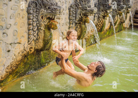 Vater und Sohn Reisende in heißen Quellen von Banjar. Das Thermalwasser wird aus dem Mund von Statuen an einem heißen Quellen von Banjar, Bali, Indonesien freigegeben Stockfoto