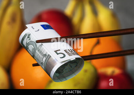 Chinese sticks halten fünf Euro auf einem Hintergrund von Essen. Konzept zum Thema der wirtschaftlichen Konfrontation zwischen Europa und China. Essen Embargo Stockfoto