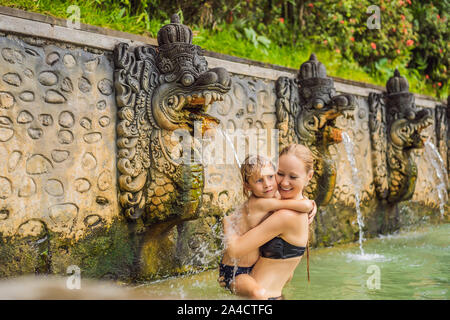 Mutter und Sohn Reisende in heißen Quellen von Banjar. Das Thermalwasser wird aus dem Mund von Statuen an einem heißen Quellen von Banjar, Bali, Indonesien freigegeben Stockfoto