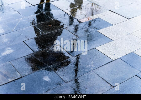 Unscharfe Reflexion Schatten Silhouette einer Frau zu Fuß unter dem Dach in einer Fußgängerzone Stadt nasse Straße in eine Pfütze, Herbst regnerischen Abend Stockfoto