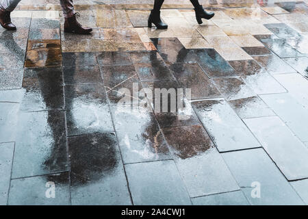 Unscharfe Reflexion Beine und Schatten, Silhouetten der Menschen in den nassen Bürgersteig, in eine Pfütze von Menschen zu Fuß auf einem Regen unter dem Dach Stockfoto