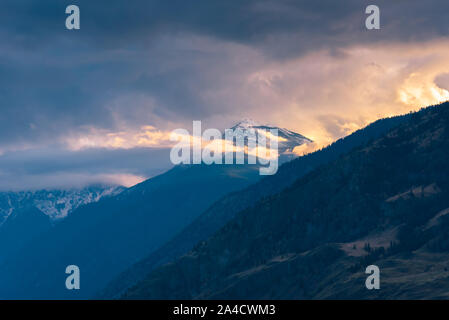 Die schneebedeckten Berge im Sonnenuntergang leuchtenden Licht mit dramatischen Wolken und Nebel im Cawston, British Columbia, Kanada Stockfoto