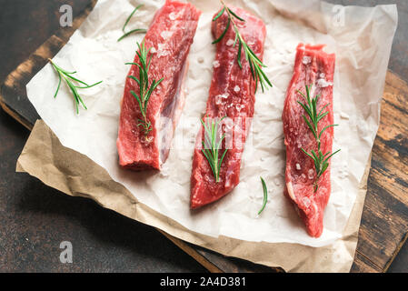 New York Strip Steak mit Salz und Rosmarin auf schwarzen Hintergrund, Ansicht von oben, aus der Nähe. Auch rohes Rindfleisch strip Steaks. Stockfoto