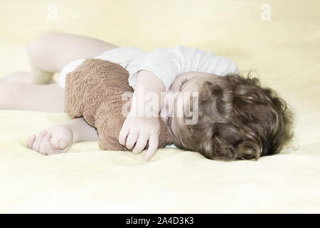 Ein kleines Kind schläft umarmt einen Teddybären, lockiges Haar kaukasischen Kind liegt in einem Plüschtier begraben, Soft Focus Stockfoto