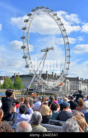 Rückansicht Gruppe von Menschen überfüllten Themse sightseeing tour Boot Touristen unter Handy Foto von ikonischen London Eye Riesenrad England Großbritannien Stockfoto