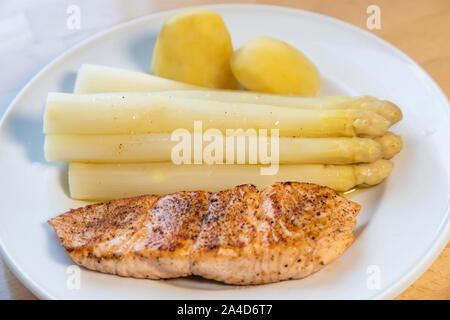 Weißer Spargel, Spargelspitzen, gekocht, mit Kartoffeln und ein gebratenes Lachsfilet, auf Platte, mit flüssiger Butter, Stockfoto