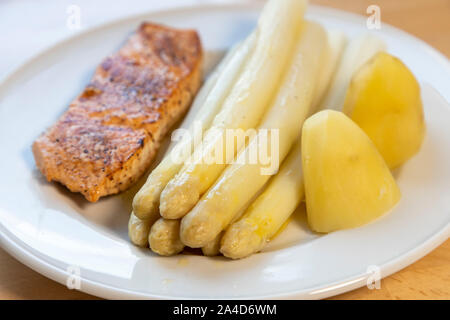 Weißer Spargel, Spargelspitzen, gekocht, mit Kartoffeln und ein gebratenes Lachsfilet, auf Platte, mit flüssiger Butter, Stockfoto