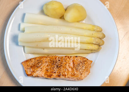 Weißer Spargel, Spargelspitzen, gekocht, mit Kartoffeln und ein gebratenes Lachsfilet, auf Platte, mit flüssiger Butter, Stockfoto