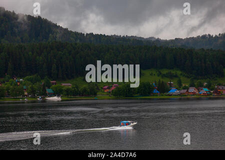 Ein Boot schwimmt auf dem Ufer, an dem es gibt grüne Bäume und andere Schiffe in den Altai Bergen zum Moor. Freizeit und Outdoor Reisen ohne Menschen. Stockfoto