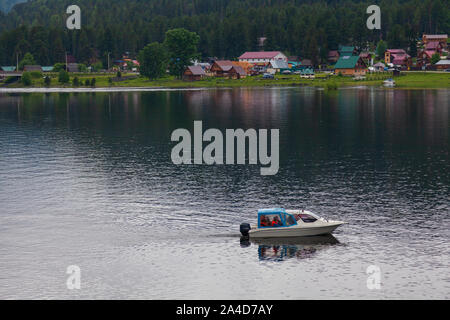 Ein Boot schwimmt auf dem Ufer, an dem es gibt grüne Bäume und andere Schiffe in den Altai Bergen zum Moor. Freizeit und Outdoor Reisen ohne Menschen. Stockfoto