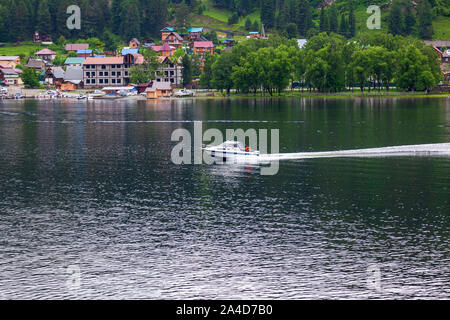Ein Boot schwimmt auf dem Ufer, an dem es gibt grüne Bäume und andere Schiffe in den Altai Bergen zum Moor. Freizeit und Outdoor Reisen ohne Menschen. Stockfoto