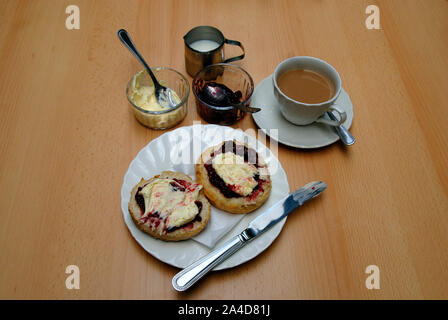 Traditioneller Nachmittagstee mit großen Scone in zwei Hälften schneiden, mit Himbeeren Marmelade und Clotted Cream auf beiden Hälften Stockfoto