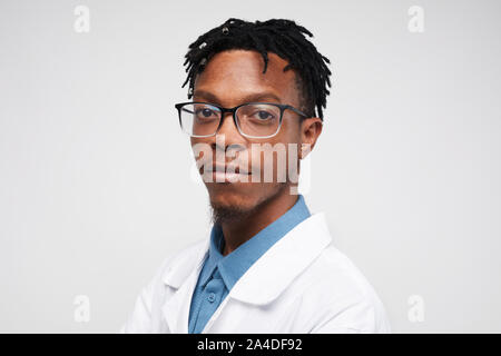 Kopf und Schultern Porträt des modernen Afro-amerikanische Mann mit Laborkittel und Kamera vor weißem Hintergrund, kopieren Raum Stockfoto