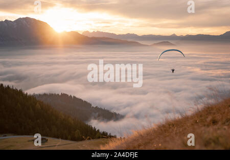 Mann Paragliding über den Wolken bei Sonnenuntergang, Salzburg, Österreich Stockfoto