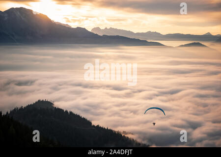 Mann Paragliding über den Wolken bei Sonnenuntergang, Salzburg, Österreich Stockfoto