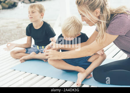 Eine Lehrerin unterrichtet junge Kinder Yoga in Posen zu tun und richtig halten die Mudras auf die Finger der Teilnehmer. Stockfoto