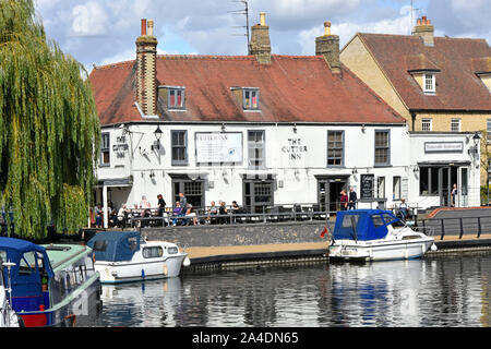 Mittag Sommer Szene Leute außerhalb der Cutter Inn Pub & Restaurant am Wasser Fluss Great Ouse Boote neben Leinpfad Ely, Cambridgeshire England Großbritannien Stockfoto