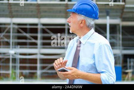 Leitender Ingenieur mit seinem Smartphone auf einer Baustelle im Freien Stockfoto