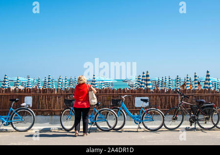 Leihfahrräder am Strand. Blaue Fahrräder auf der Straße. Viele Sonnenschirme. Stockfoto