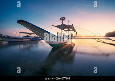 El Nido, Palawan, Philippinen. Traditionelle banca Boot in die Badebucht im goldenen Abendlicht. Ruhigen malerischen bacuit Archipel Inseln am Horizont Stockfoto