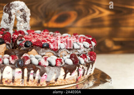 Eine Nahaufnahme eines Vegane Schokoladentorte mit Himbeeren und Blaubeeren bedeckt, in den Kühlschrank eingefroren, auf einem Tisch mit verschwommenen Hintergrund. Kopieren Stockfoto