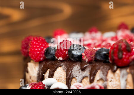 Eine Nahaufnahme eines Vegane Schokoladentorte mit Himbeeren und Blaubeeren bedeckt, in den Kühlschrank eingefroren, auf einem Tisch mit verschwommenen Hintergrund. Kopieren Stockfoto