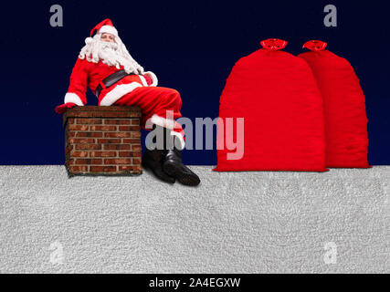 Santa Claus sitzt auf dem Schornstein an einem verschneiten Dach mit großen Taschen voller Weihnachtsgeschenke, Hintergrund von dunklem Blau mit Sternen. Stockfoto