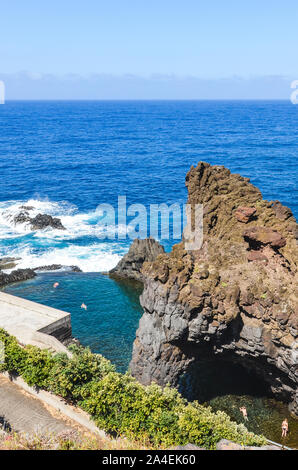 Touristen Baden in natürlichen Pools in den Atlantischen Ozean in Seixal, Madeira, Portugal. Pool von vulkanischen Gesteinen aus dem offenen Meer umgeben. Blick von oben. Sommer Urlaub. Stockfoto